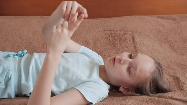 Nice girl lying on bed and playing with fingers. Lovely young girl having fun at home. Leisure concept