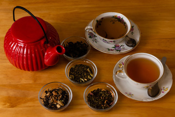 Tetera rojo oriental con distintos tipos de té en hebras,  sobre mesa de madera moderna y con 2...