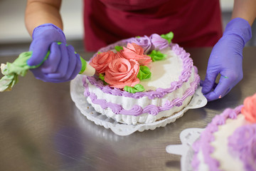 Pastry chef decorates the cake with flowers from the cream.  The cream is squeezed out of the pastry bag through a special nozzle
