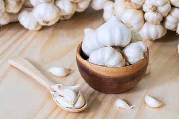 Garlic bulbs in wooden bowl and garlic cloves in wooden spoon on wooden table with garlics blur background..