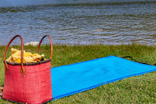 Beach mat and bag on green grass near the lake.