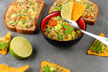 Mexican nachos corn chips with guacamole avocado sauce. Vegan nachos snack, lime on stone board. Healthy food.