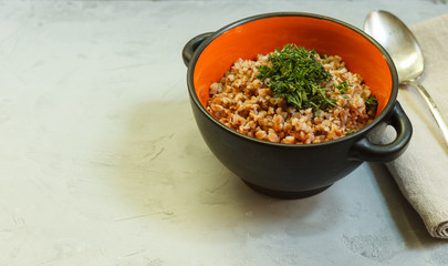 Buckwheat porridge in a black and orange bowl with greens on a gray background with space