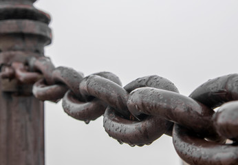 An iron chain on a pier on a cloudy, foggy morning covered in drops of water.