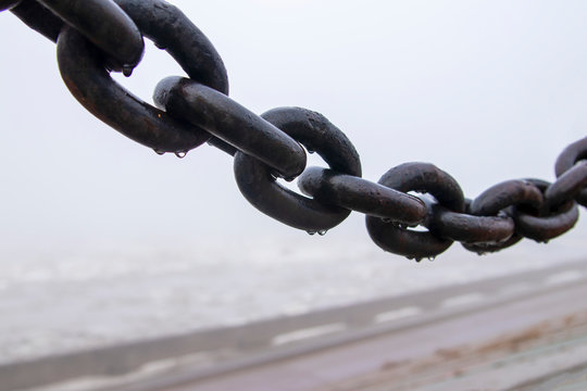 An iron chain on a pier on a cloudy, foggy morning covered in drops of water.