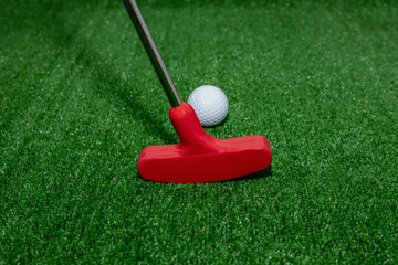 Mini golf. A club and a white ball on a golf course.