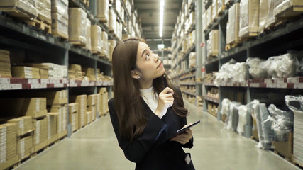 Asian female worker wearing a black suit Checking in warehouse For her company To export to customers By using pens and tablets for note-taking..