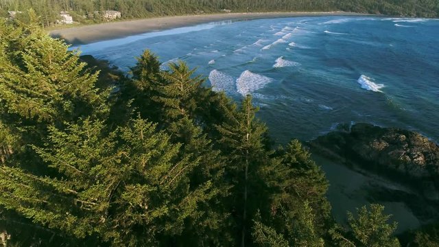Cinematic aerial reveal shot of waves crashing onto beach with lush, temperate wilderness in the background, sun set. Summer day, West Coast coastline. West Coast, Tofino, Vancouver, Canada.