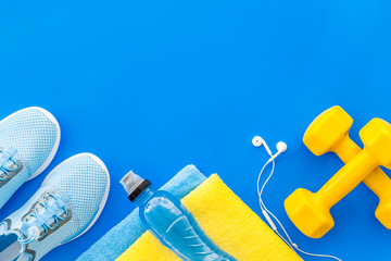 Fitness equipment. Sneakers, dumbbells, headphones on blue background top view copy space
