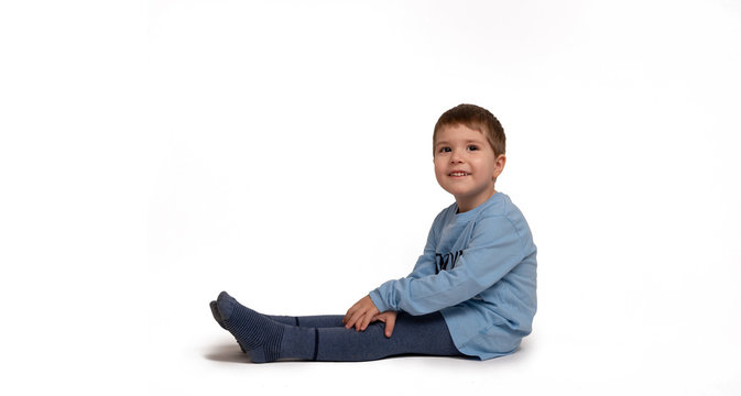 Little boy in blue T-shirt sits on the floor against a white background