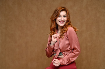 Horizontal portrait of a happy woman with a smile with long red hair in a pink blouse. Photo taken in the studio on a beige background.