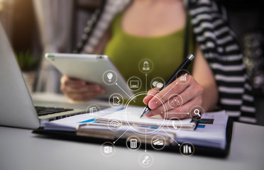 Businesswoman or Designer using tablet with laptop and document on desk in modern office with virtual interface graphic icons network diagram.