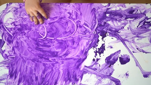Close up top view of baby toddler hand making mess with purple paint on the table. 