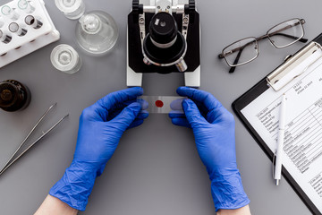 Research with microscope, hands hold blood sample. Grey table top view