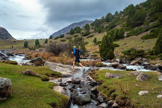 A guy jogs across a mountain river. Man training outdoors. Sky running