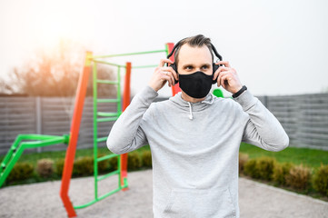 Young guy in a medical mask on the playground outdoors. The guy keeps himself in good shape during...