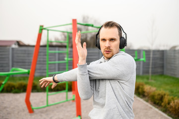 Athletic guy in a hoodie does upper body stretching and warming up before a workout outdoors. Training on the sports ground. Healthy lifestyle concept