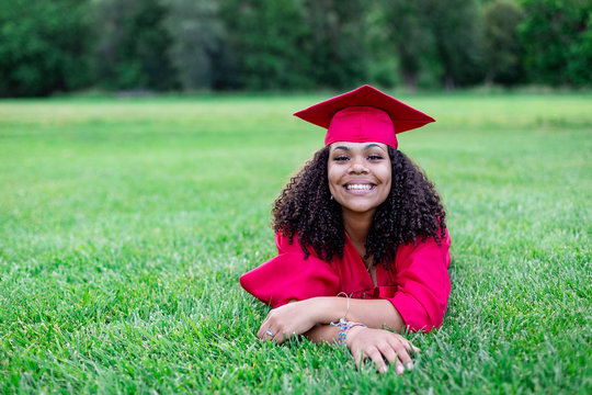 Portrait of a beautiful multiethnic woman in her graduation cap and gown. Smiling and cheerful as she poses lying down in the grass