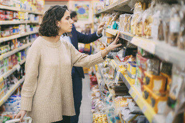 Serious woman looking at cookies in grocery store. Side view of people choosing baked goods in supermarket, selective focus. Shopping concept