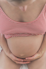 Pregnant woman sitting at home on bed holding belly