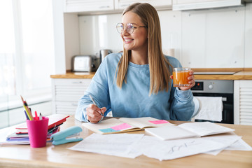 Image of woman drinking juice while studying with exercise books