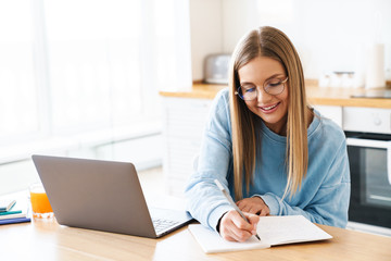 Image of woman making notes in planner while working with laptop