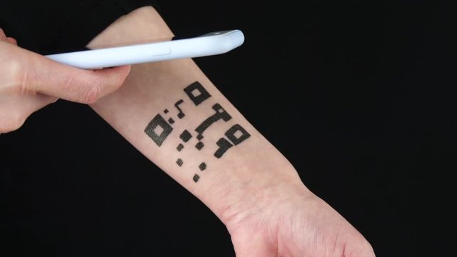 A woman reads the barcode using a smartphone camera. Abstract tattoo on the body, hand with a QR code pattern. The concept of control of personal data.