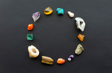 Beautiful multi-colored gems and crystals are arranged in a circle in the form of a rounded frame or wreath on a black contrasting background for posts in social networks and sales ads.