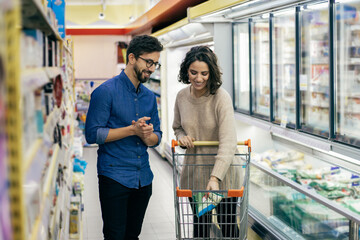 Smiling couple buying products in grocery store. Happy young man and woman with shopping trolley...