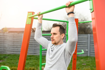 A young man is working on a horizontal bar outdoors, he is doing pull-ups. Healthy lifestyle concept