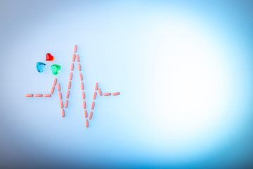 Pills in shape of cardiogram pulse on blue gradient background. Pink vitamins and glass hearts, symbol of healthy lifestyle. light copy space. Heartbeat rhythm made of tablets