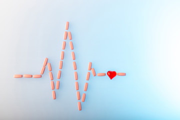 Pills in shape of cardiogram pulse on blue gradient background. Vitamins and red glass heart, symbol of healthy lifestyle. Pharmaceutical and cardiology concept. Heartbeat rhythm made of tablets