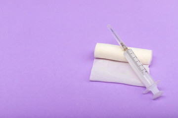 Medical bandage and syringe on a lilac background. A gauze roll on which the syringe lies. Dressing for medical purposes. Space for text on the left.