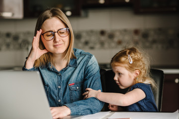Woman working, learns on laptop computer. A young mother on a childcare leave works at home and daughter distracts her. Freelance. Writing, typing. Communication and technology concept. Paperwork.