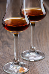 two glasses of sniffer with cognac and waves and splash closeup on wooden background