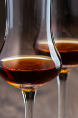 two glasses of sniffer with cognac and waves and splash closeup on wooden background