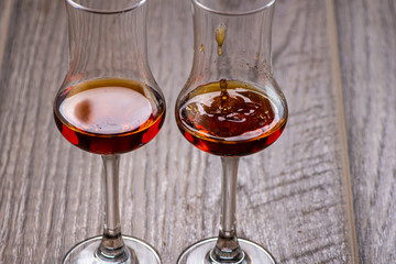 two glasses of sniffer with cognac and waves and splash closeup on wooden background