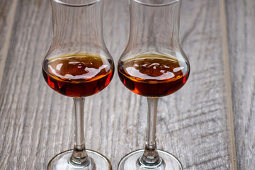 two glasses of sniffer with cognac and waves and splash closeup on wooden background