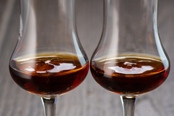 two glasses of sniffer with cognac and waves and splash closeup on wooden background