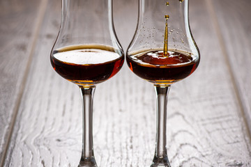 two glasses of sniffer with cognac and waves and splash closeup on wooden background