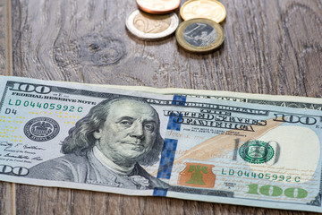 Euro coins and one hundred dollars on a wooden background