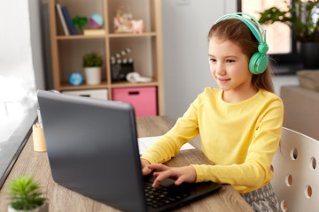 children, education and distant learning concept - little student girl in headphones with laptop computer at home