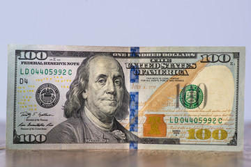 one hundred dollar bill with a lit face on a wooden background