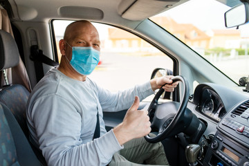 A man in a protective mask driving a car. Portrait of a man in a car in a surgical mask. A man goes to rest in the countryside.