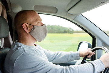 A man in a protective mask driving a car. Portrait of a man in a car in a surgical mask. A man goes to rest in the countryside.