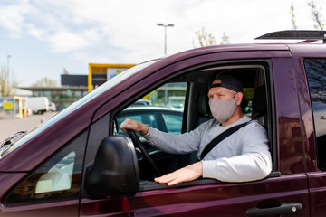 A man in a protective mask driving a car. Portrait of a man in a car in a surgical mask. A man goes to rest in the countryside.
