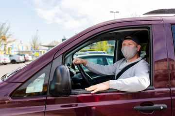 A man in a protective mask driving a car. Portrait of a man in a car in a surgical mask. A man goes to rest in the countryside.