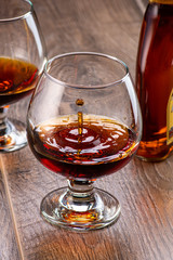 two glasses with cognac and splash next to a bottle on a wooden background