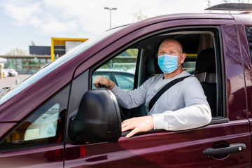 A man in a protective mask driving a car. Portrait of a man in a car in a surgical mask. A man goes to rest in the countryside.