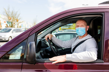 A man in a protective mask driving a car. Portrait of a man in a car in a surgical mask. A man goes to rest in the countryside.